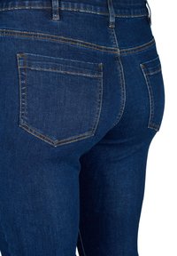 Jeans in denim blu scuro con vita alta, dotati di due tasche posteriori e cuciture arancioni a contrasto lungo le cuciture e i bordi delle tasche.