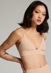Naakt bralette met een diepe V-hals, minimalistische banden en een soepele, rekbare textuur voor een comfortabele pasvorm.