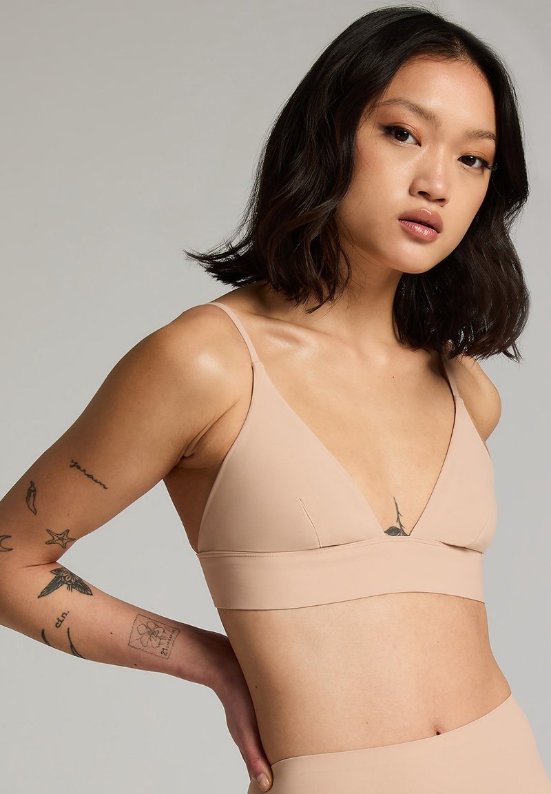 Naakt bralette met een diepe V-hals, minimalistische banden en een soepele, rekbare textuur voor een comfortabele pasvorm.