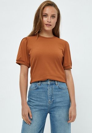 Smešasti smeđi kratki rukav T-shirt s okruglim izrezom i napuhanim rukavima, uparen s plavim trapericama viskog struka.