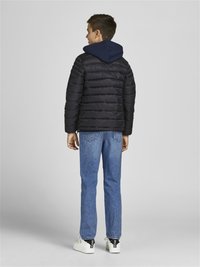 Giacca a pipistrello nera con cuciture orizzontali, cappuccio blu e colletto alto, abbinata a jeans blu e sneakers bianche.