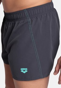 Costumi da bagno grigio scuro realizzati in tessuto leggero, dotati di una vita elasticizzata, cuciture turchesi e un piccolo logo "arena" sul lato.