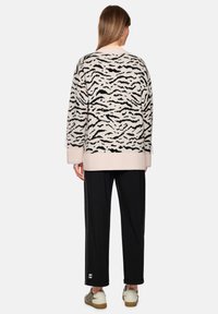 Cremefarbener Pullover mit schwarzem Tigermuster, gerippten Bündchen und Saum. Kombiniert mit schwarzer Hose und gemusterten Schuhen.