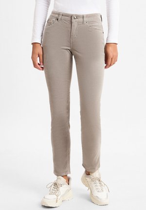 Beige enganliegende Jeans mit glatter Textur, gesteppten Details an den Nähten, fünf Taschen und einem Knopfverschluss, kombiniert mit cremigen Sneakers.