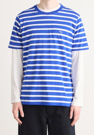 Personne portant une chemise à manches courtes rayée horizontale bleu et blanc par-dessus une chemise blanche à manches longues avec un pantalon noir.