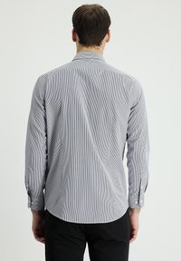 Camisa de manga larga a rayas grises y blancas, con puños abotonados, corte entallado, dobladillo curvado, tejido suave y detalle en la yugo de la espalda.