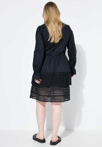 Vestido negro con mangas largas, diseño en capas y acentos de encaje. La parte superior tiene un corsé ajustado y la falda en capas presenta encaje transparente.