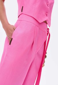 Roze op maat gemaakte broeken met een gladde textuur, geplooide voorkant, zijzakken en een bijpassende tailleband met strik voor een verstelbare pasvorm.