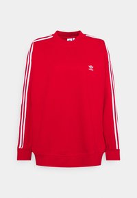 Röd sweatshirt med hög krage, vita tre-stripes accenter längs ärmarna och en liten vit logotyp på bröstet. Mjuk tygtextur.