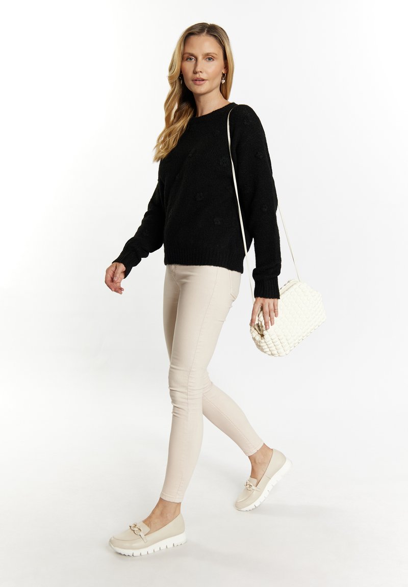 Sort strikket sweater med hævede blomsterapasninger, parret med lysebeige skinny bukser. Hvid tekstureret håndtaske og beige slip-on sko.