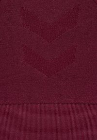 Gros plan d’un tissu tricoté lie de vin avec deux motifs chevrons texturés et un ourlet côtelé en bas.
