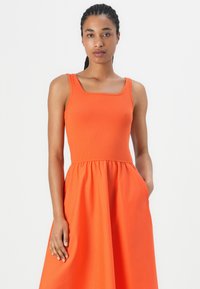 Orange dress featuring a ribbed bodice with square neckline and a flowing skirt. Includes pockets and a smooth texture.