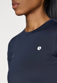 Tengerészkék, testhezálló póló kerek nyakkivágással, bal mellrészen fehér logóval. Az anyag simának és kissé rugalmasnak tűnik.