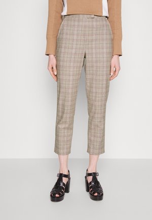 Personne portant un pantalon court à carreaux beige et rose avec des sandales noires à talons et un haut à manches longues couleur chameau.