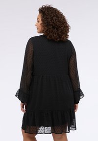Vestido negro con un dobladillo con volantes, mangas abullonadas y textura de puntos. La vista trasera revela un ajuste relajado y un diseño fluido.