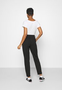 Pantalon noir ajusté avec une taille haute et une texture lisse, associé à un t-shirt blanc à manches courtes.