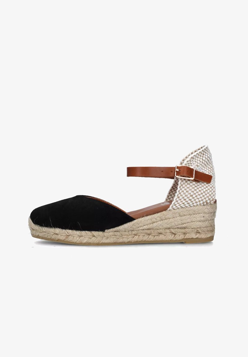 Espadrille cuña de ante negro con una correa de cuero marrón en el tobillo, tejido beige en la parte posterior y suela de yute texturizada.