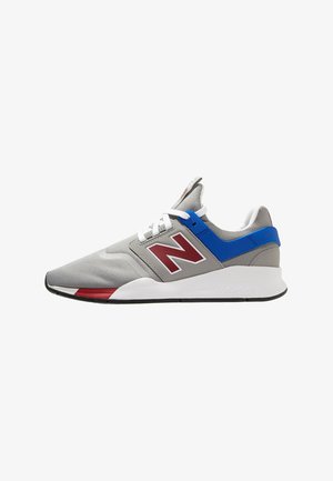 Chaussure de sport grise avec lacets blancs, logo rouge "N", bride bleu au talon, et semelle blanche avec accents rouges et noirs.