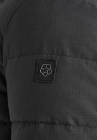 Schwarze gepolsterte Jacke mit glatter Textur, ausgestattet mit einem sternförmigen Logo-Patch und genähten Details auf der Schulter.