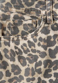 Tejido de denim con estampado de leopardo en tonos beige y negro. Presenta un bolsillo frontal y costuras marrones a lo largo de las costuras. Acabado texturizado.