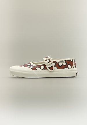 Zapato Mary Jane de Vans Single con base marrón, patrón de margaritas blancas y negras, suela blanca y correa ajustable con hebilla sobre fondo neutro.