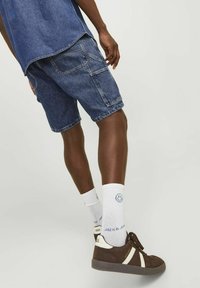 Shorts de mezclilla en azul oscuro con un ajuste relajado, bolsillos visibles, combinados con zapatillas marrones y calcetines blancos con un diseño de carita sonriente.
