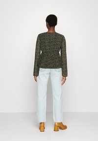 Blusa preta com padrão floral, de mangas longas, design peplum e decote redondo. Combinada com jeans azuis claros de perna reta e sapatos de salto bloco castanhos.