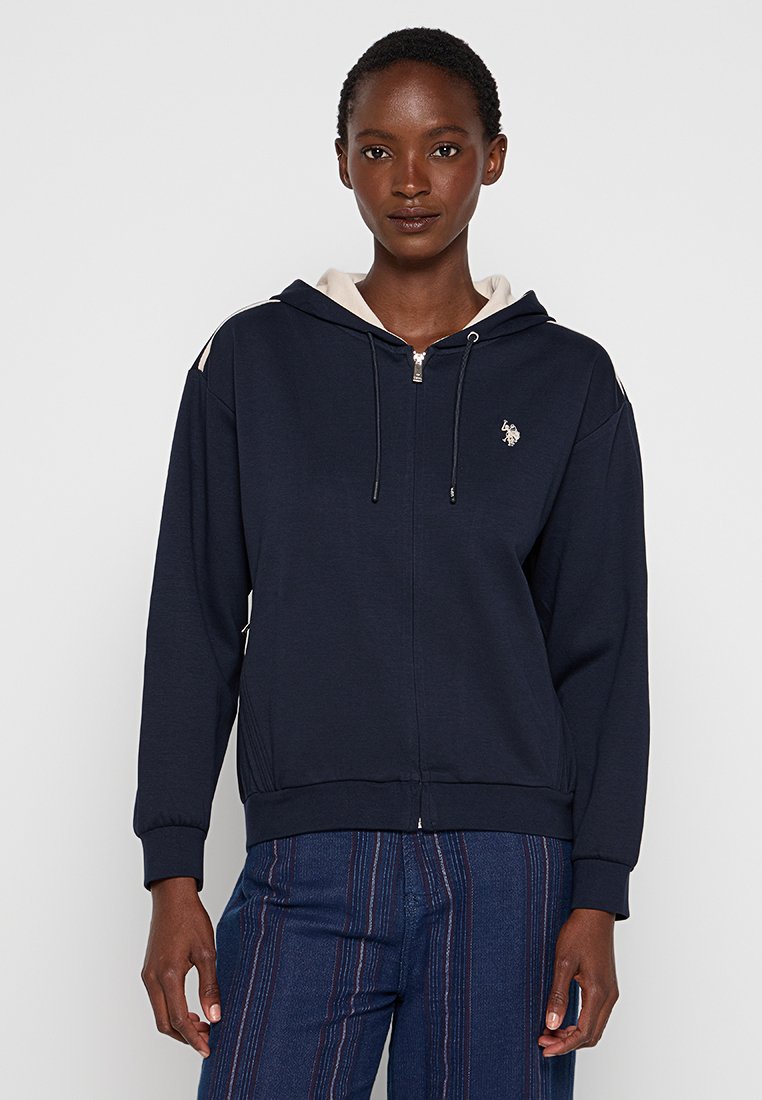 Marineblauwe zip-up hoodie met een contrasterende beige capuchon, koordjes en klein geborduurd logo. Bevat ribbelstof aan de mouwen en onderrand voor een getailleerde look.