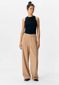 Sort ribbet tank top og beige brede bukser med frontfolder. Bukserne har høj talje og sidelommer. Sorte sko.