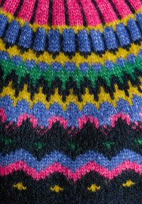 Úsek pleteného svetra s viacfarebným vzorom v ružovej, modrej, žltej, zelenej a čiernej farbe, zobrazujúci žigzagové a chevronové vzory.