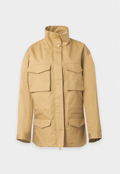 Veste légère beige avec col montant, fermeture éclair sur le devant avec boutons-pression et quatre poches à rabat devant.
