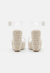 Sandalias de tacón transparente con plataforma de yute trenzado, adornadas con detalles plateados y una correa de tobillo transparente. Diseño de tacón alto y bloque.