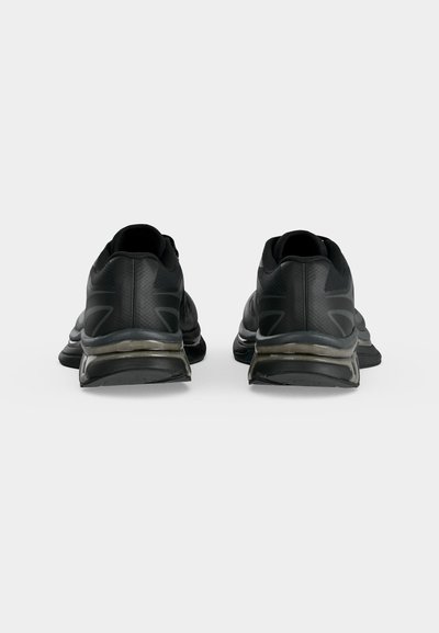 Ζευγάρι μαύρα αθλητικά παπούτσια εμφανιζόμενα από πίσω, με μαξιλαρωμένες σόλες και διακριτικά σχεδιαστικά στοιχεία σε λευκό φόντο.
