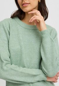 Hellgrüner gestrickter Pullover mit runden Halsausschnitt und gerippten Bündchen, der eine weiche Textur und einen lässigen Schnitt zeigt.