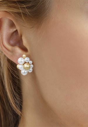 Orecchino a perno con grappolo di perle bianche e dorate indossato all'orecchio sinistro, mostrando pelle chiara e capelli fini castano chiaro dietro l'orecchio.