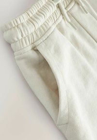 Hellebeige Jogginghose mit Kordelzug, elastischem Rippbund, seitlichen Taschen und glatter Stoffstruktur mit dezenten Nahtdetails.