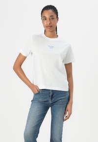 White short-sleeve t-shirt made of cotton, featuring a small blue graphic that says "ICE CREAM PLEASE," paired with blue jeans.