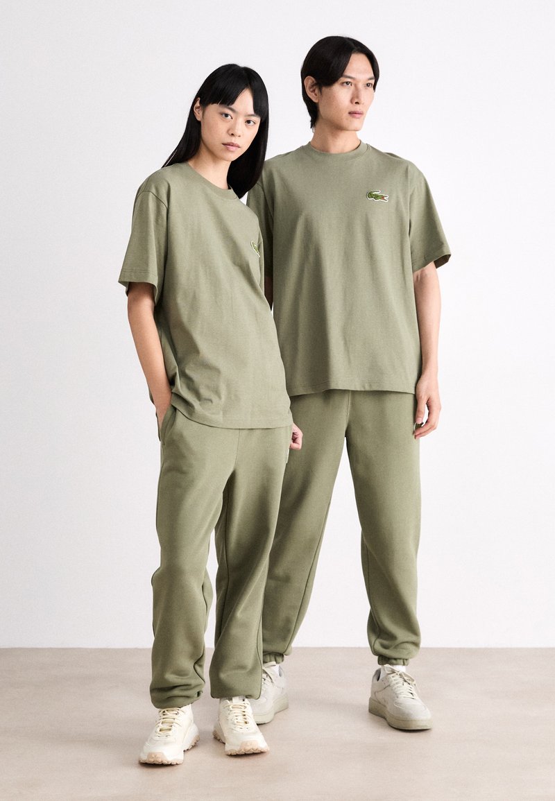 Groene katoenen T-shirts met een ontspannen pasvorm, gecombineerd met bijpassende joggers. Beide outfits hebben een minimalistisch ontwerp en een geborduurd logo.