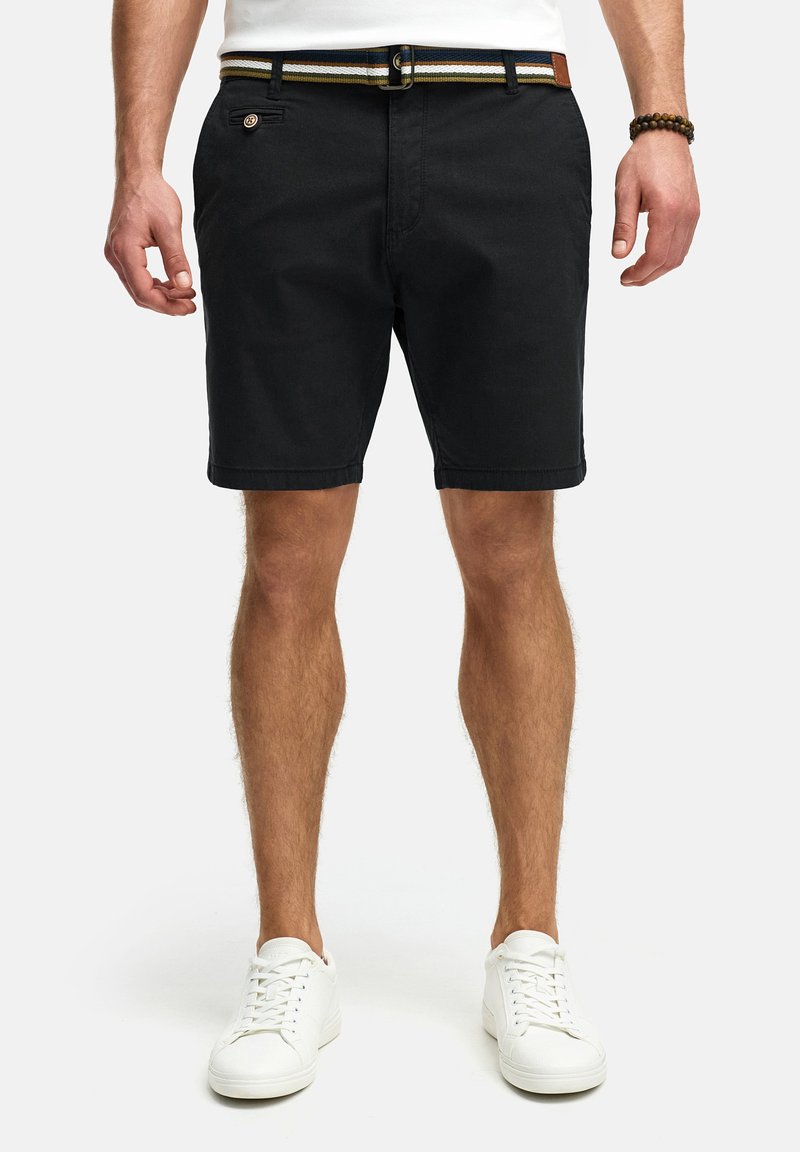 Schwarze Shorts aus Baumwolle mit flachem Vorderteil, seitlichen und hinteren Taschen, ausgestattet mit einem gestreiften Gürtel mit Lederdetails, kombiniert mit weißen Sneakers.