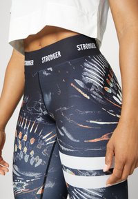 Højderede, marineblå leggings med et trykt design, der har abstrakte mønstre og hvide striber. Fremstillet af strækbart, åndbart materiale.