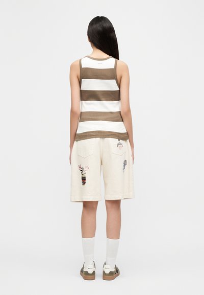 Débardeur rayé marron et blanc, associé à un short ample crème orné de motifs brodés colorés et à des baskets plates. Chaussettes blanches visibles.