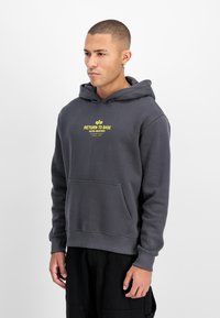 Harmaa huppari, jossa on etutasku ja keltainen graafinen painatus. Valmistettu pehmeästä kankaasta, jossa on resorit hihansuissa ja helmassa.