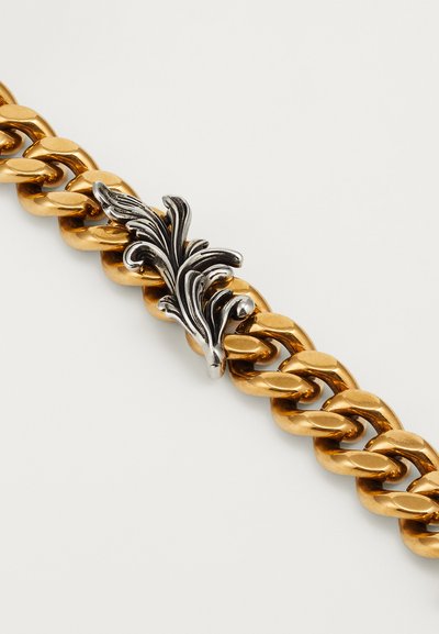 Goldene Kettenarmband mit großen Gliedern, das in der Mitte mit einem silbernen, kunstvoll verzierten Akzent hervorsticht, der ein detailliertes florales Design zeigt.