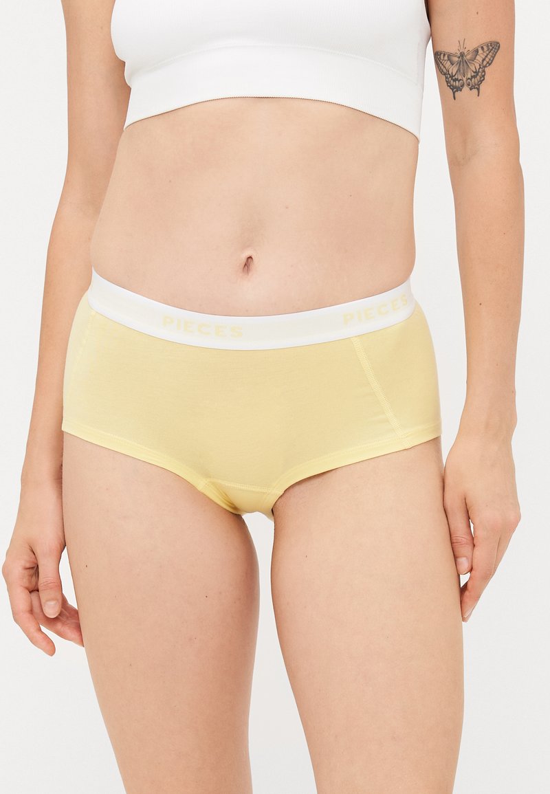 Żółta hipsterska bielizna wykonana z miękkiego materiału, z białym elastycznym pasem w logo 'PIECES' oraz gładkim, bezszwowym fasonem.