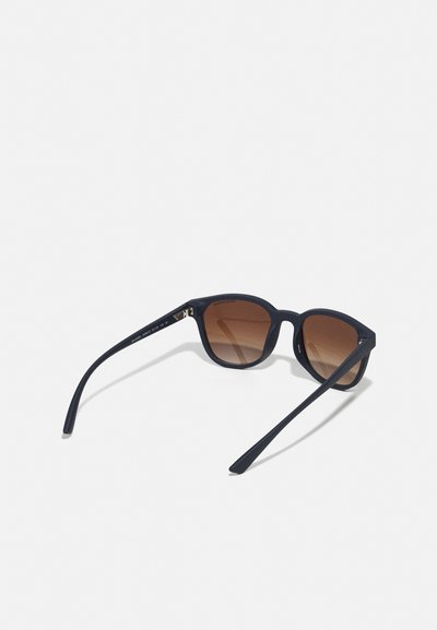 Ochelari de soare din plastic negru, cu o formă rotundă, lentile într-o nuanță de maro degradat și brațe subțiri. Prezintă detalii cu logo pe lateral.