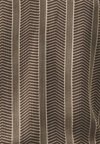 Mønstret stoff i brun og krem med sikksakk- og stripe-design. Teksturen fremstår glatt med vertikale folder synlige.