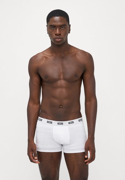 White cotton boxer briefs with a black GCDS logo waistband. The fabric is smooth, and the design features a fitted shape.