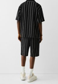 Black and white striped short-sleeve shirt and shorts set, made from textured fabric, paired with white socks and beige sneakers.