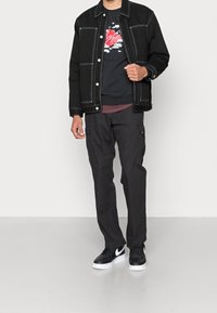 Black denim jacket with white stitching, black graphic t-shirt, dark cargo pants, and black sneakers with white soles.