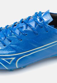 Scarpini da calcio blu con una tomaia sintetica testurizzata, dettagli gialli e bianchi a contrasto e lacci blu. Presenta tacchetti stampati sulla suola.